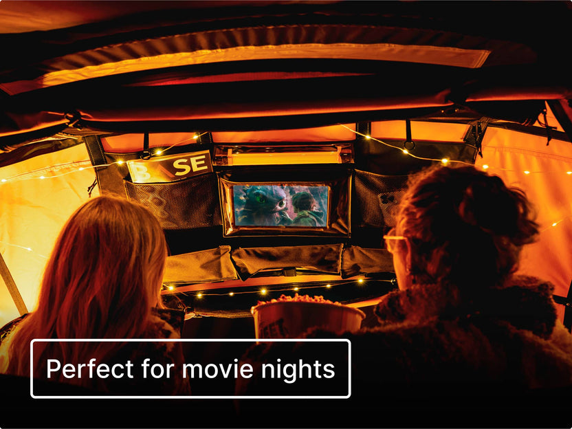 Two people inside a cosy TentBox with string lights, watching a movie on a tablet hanging from the Lite Storage Pockets. Text reads 'perfect for movie nights'.