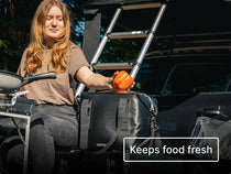 Person using a KitchenBox in front of a TentBox, placing an orange pepper inside the TentBox CoolBag.