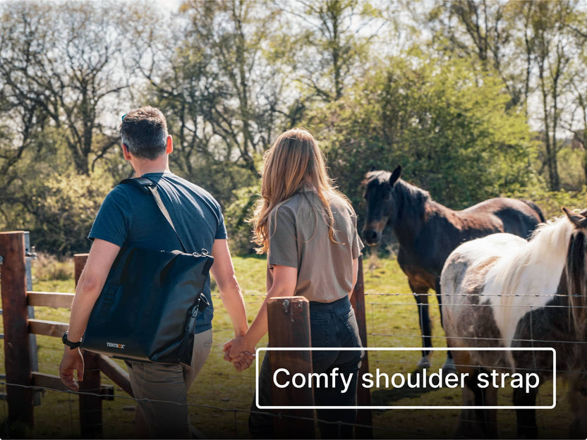 Two people walking in the countryside with horses in the background, one carrying the TentBox CoolBag with text highlighting a 'comfy shoulder strap'.