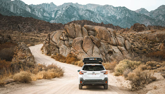 A TentBox mounted on a white SUV driving through a canyon in the USA