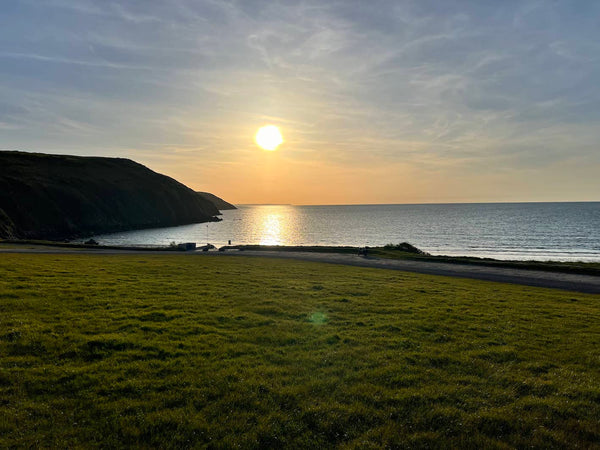 The sun setting over coastal views with a green field and blue sky