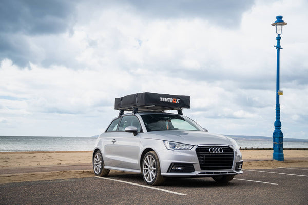 Silver Audi A1 parked by the beach with a closed TentBox roof tent mounted on top