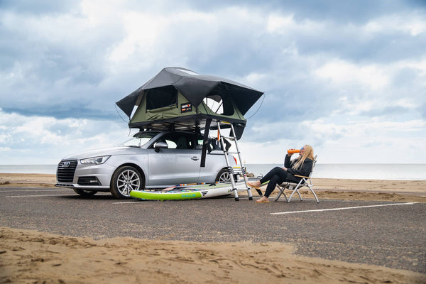 Forest Green TentBox Lite 2.0 sitting on top of an Audi A1 in a car park by the beach